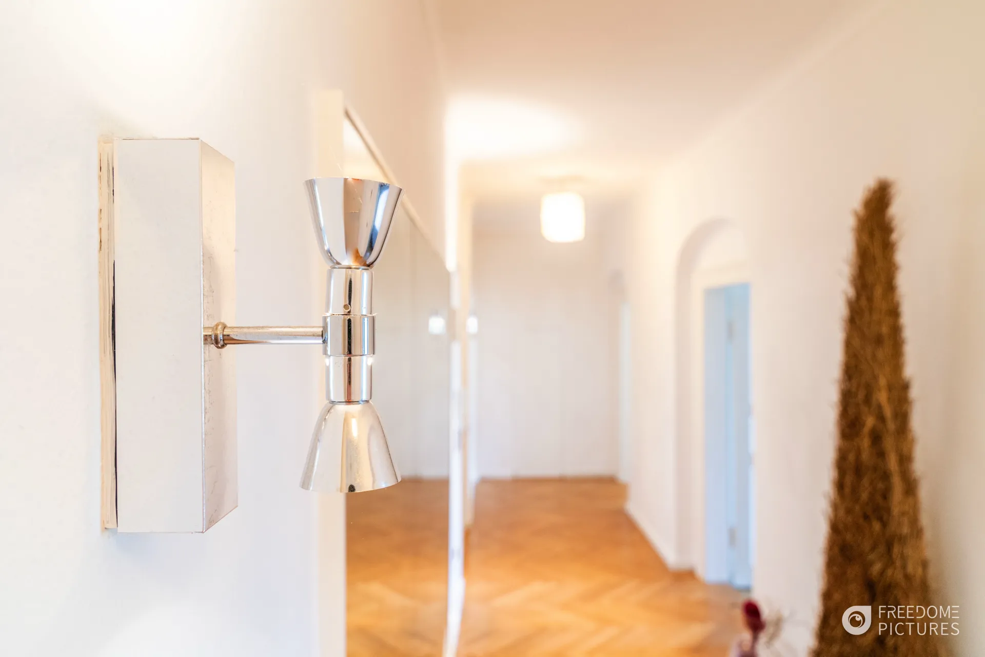 Nahaufnahme einer modernen Wandleuchte mit warmem Licht vor einem hellen, unscharfen Flur im Hintergrund