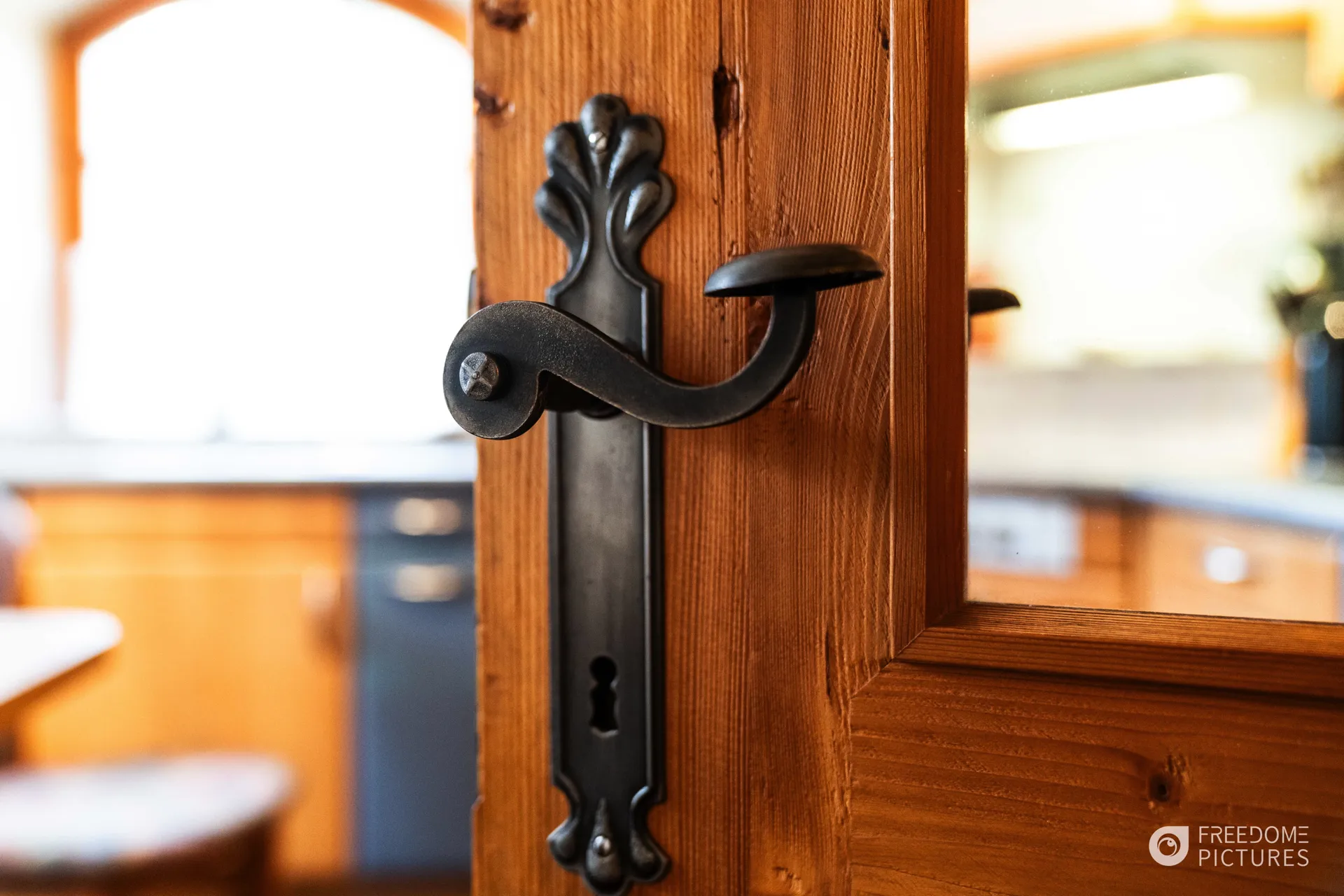 Rustikaler schmiedeeiserner Türgriff an einer Holztür mit Blick in eine Landhausküche
