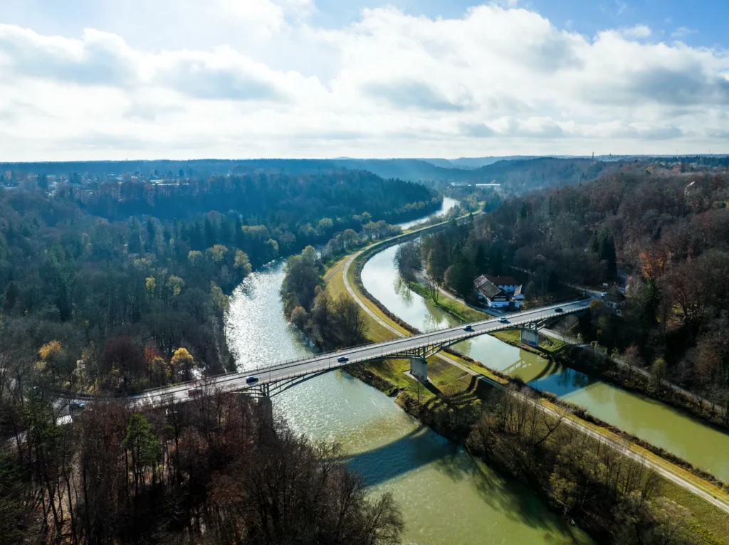 Drohnenaufnahme des Isartals bei Grünwald mit Brücke, Fluss und dichtem Baumbestand auf beiden Uferseiten