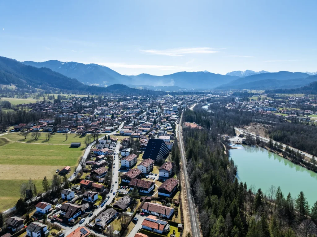Drohnenaufnahme von Lenggries mit Blick über die Isar, den Ort und das Brauneck-Massiv im Hintergrund bei blauem Himmel